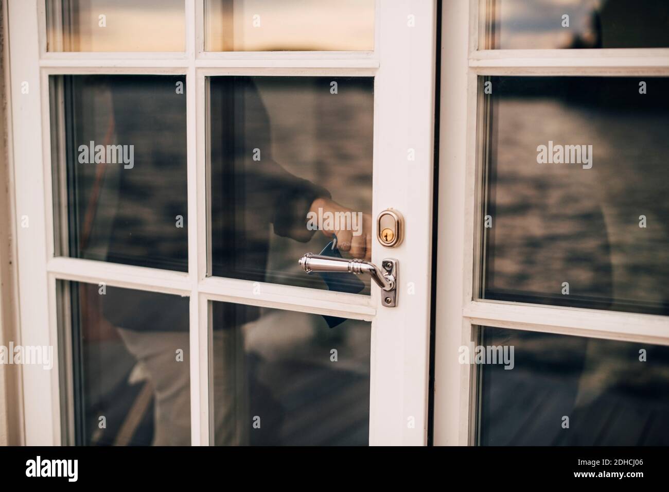 Sección central de la mujer cerrando puerta de vidrio en la villa de vacaciones Foto de stock
