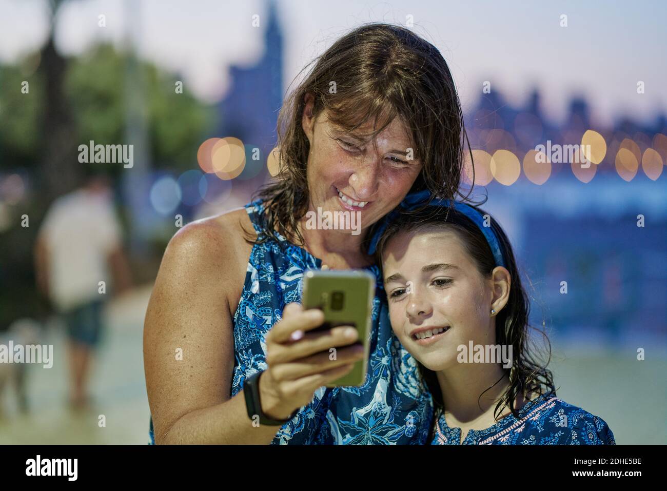 Retrato de madre e hija adolescente con vestidos azules y mirando al móvil  por la noche con una playa en el fondo. Concepto de tecnología Fotografía  de stock - Alamy