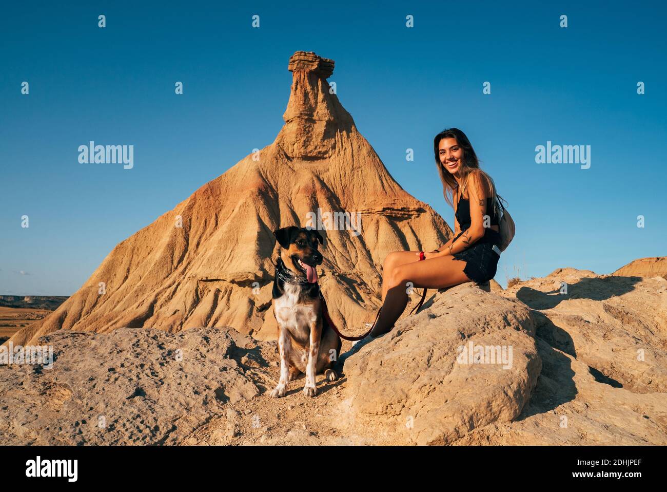 Vista lateral de encantadora mujer sentada con un perro amable rock en Bardenas  reales y mirar la cámara mientras disfruta aventura de verano Fotografía de  stock - Alamy