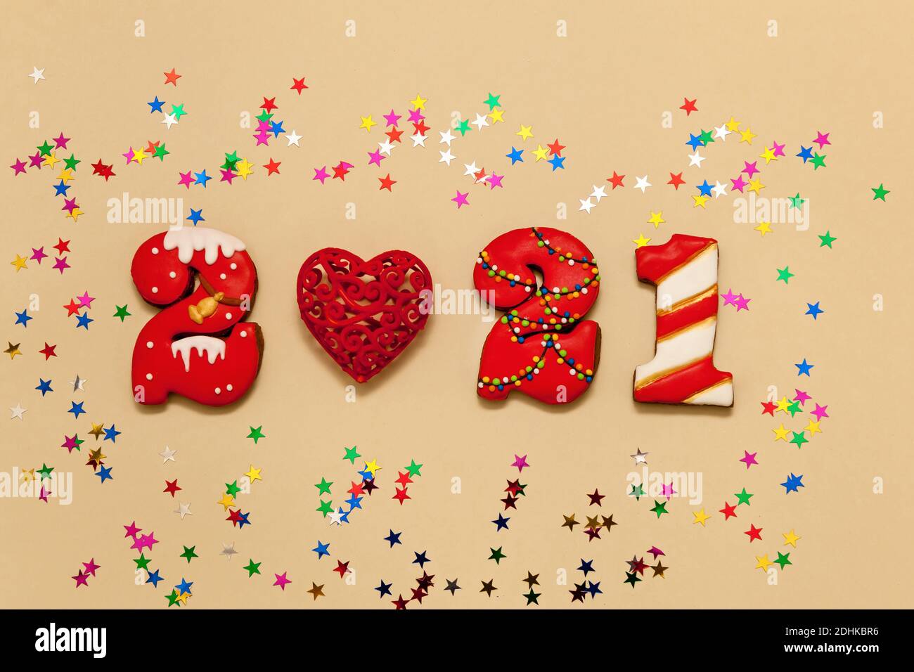 Números 2021 hechos de galletas de pan de jengibre en esmalte multicolor sobre un fondo beige. Corazón rojo y estrellas multicolor. Año nuevo 2021, Navidad h Foto de stock