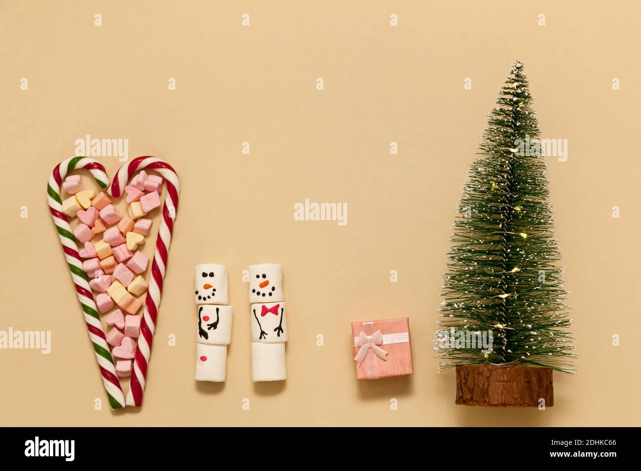 Lollipops a rayas en forma de corazón con malvaviscos sobre un fondo beige. Muñecos de nieve de malvaviscos y un árbol de Navidad. Concepto de Navidad, Feliz Nueva y Foto de stock