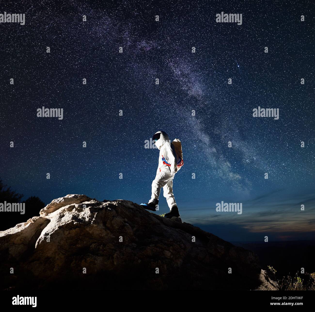 Viajero espacial escalando montaña rocosa bajo el impresionante cielo  nocturno con estrellas y vía Láctea. Astronauta en traje espacial que llega  a la cima de la roca enorme. Concepto de exploración espacial