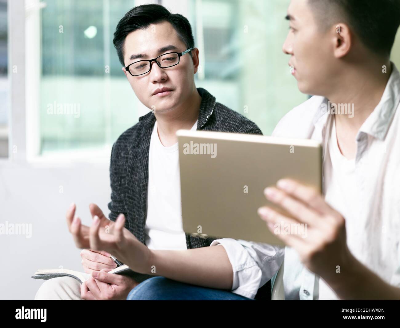 dos jóvenes empresarios asiáticos que hablan de negocios en la oficina utilizando la tecnología digital tableta Foto de stock
