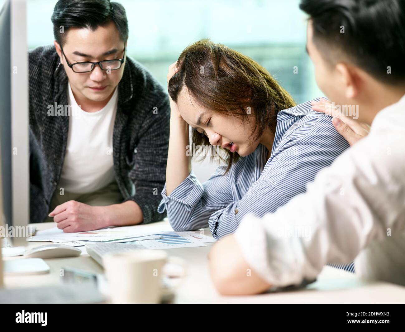 una empresaria asiática frustrada que se sienta cómoda por parte de sus colegas mientras habla de negocios en la oficina Foto de stock