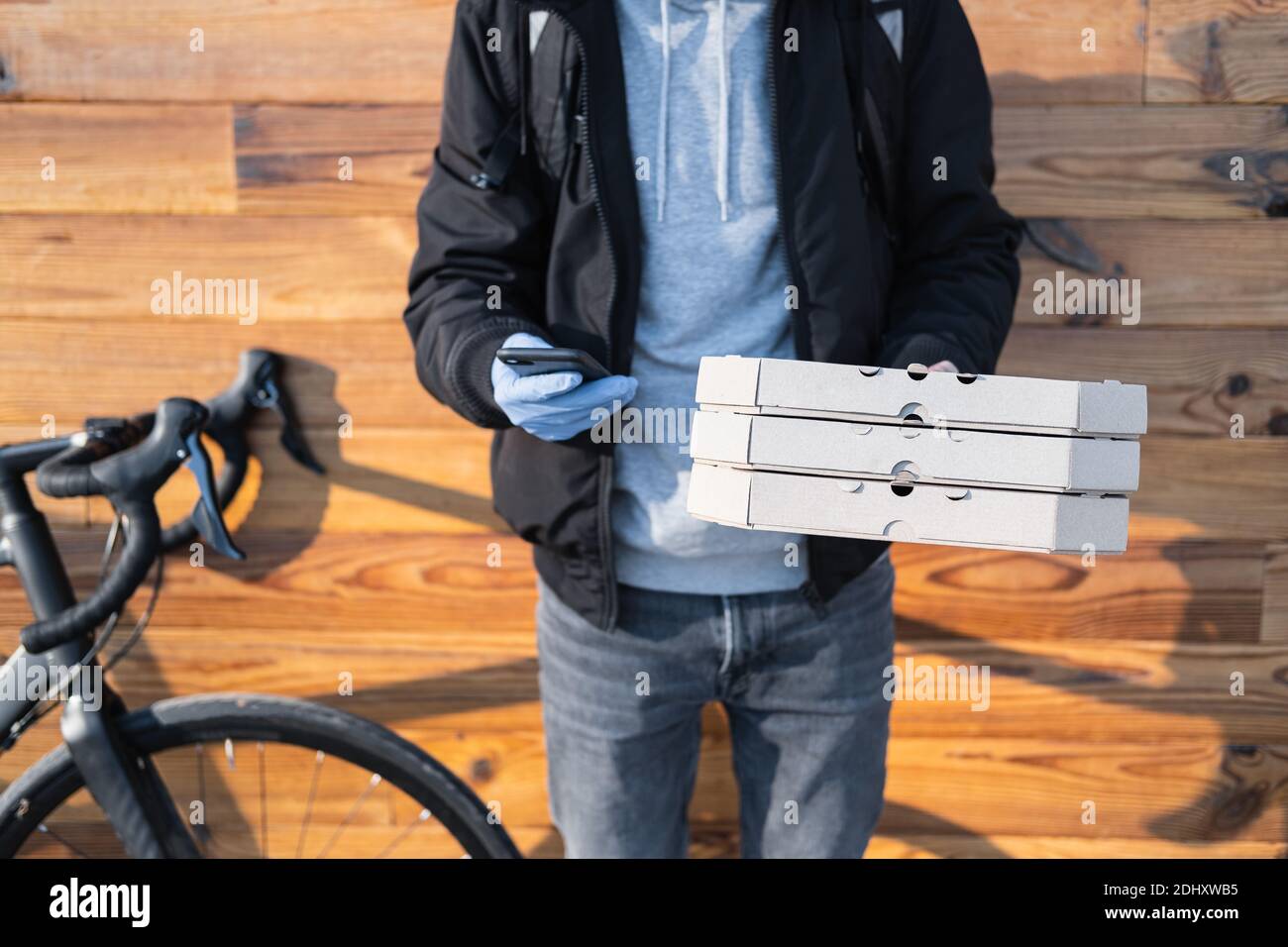 La persona encargada de la entrega junto a una bicicleta tiene cajas de  pizza y un teléfono. Trabajo como mensajero, profesión de mensajero de  bicicleta, concepto de trabajo a tiempo parcial Fotografía