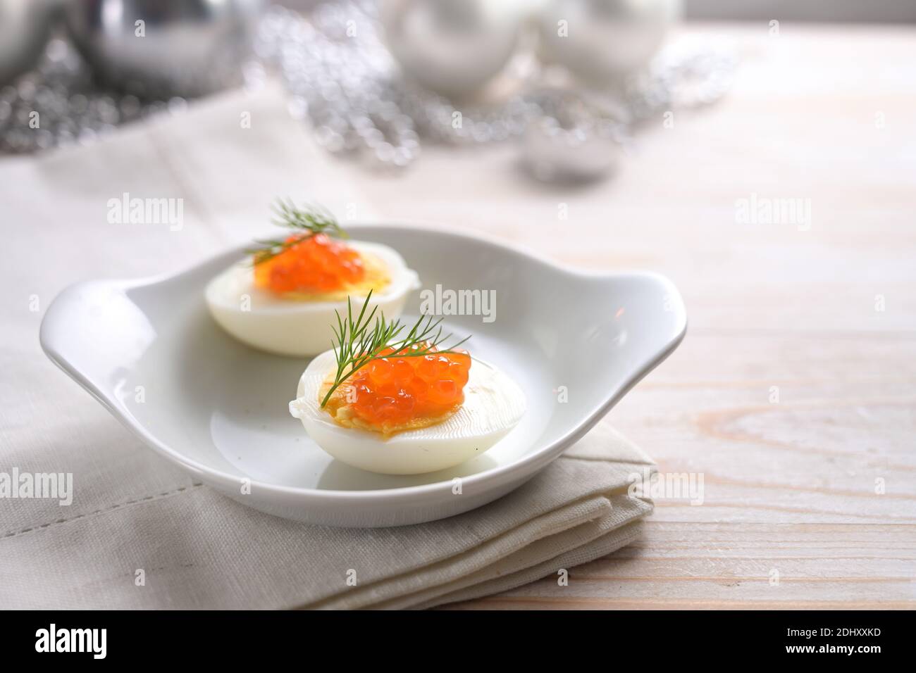 Huevos a la mitad con caviar rojo y guarnición de eneldo en una mesa de madera gris claro con decoración navideña, aperitivo festivo para una fiesta de vacaciones, espacio de copia, se Foto de stock