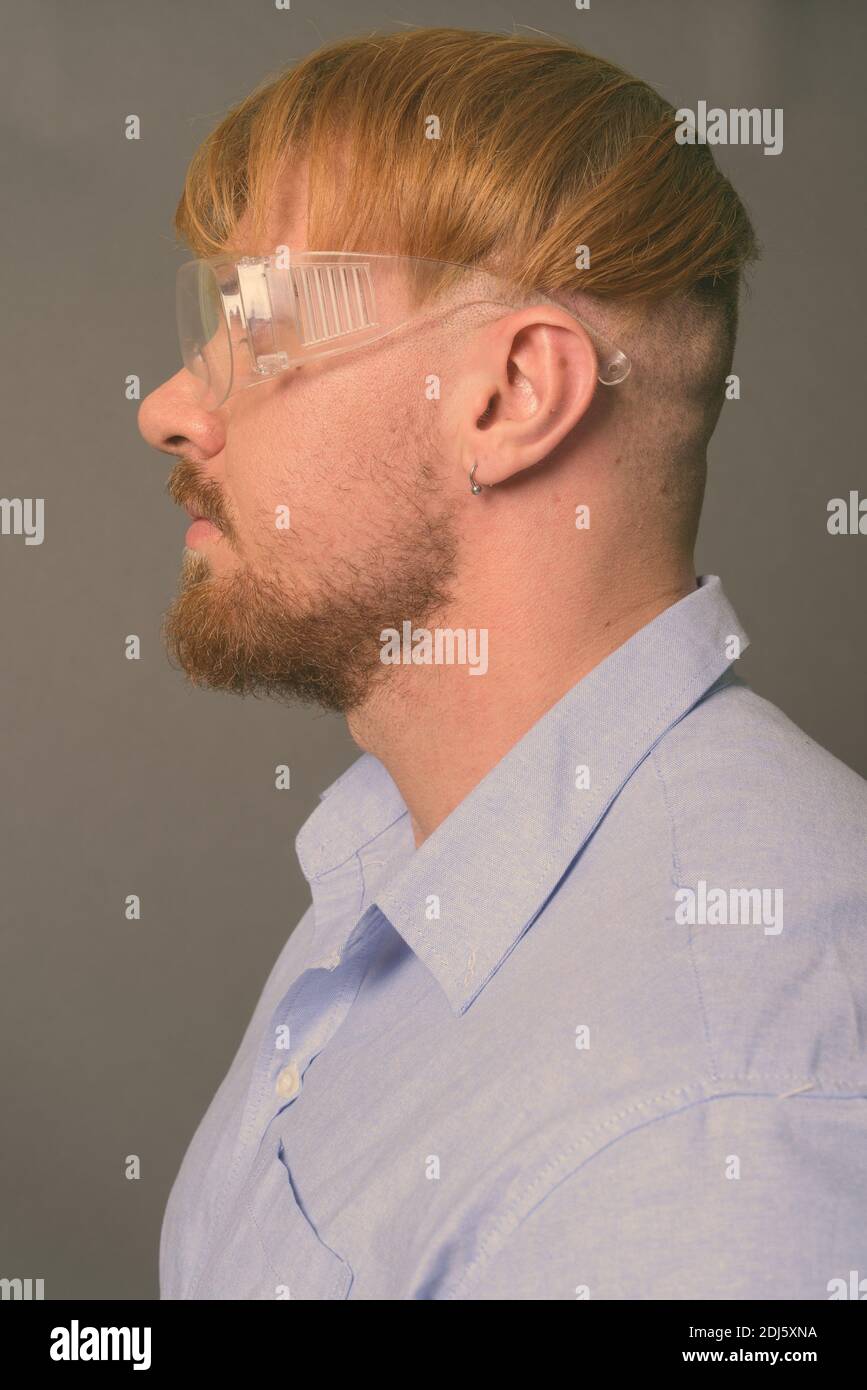 Hombre bearded doctor con pelo rubio usando gafas de protección contra fondo gris Foto de stock