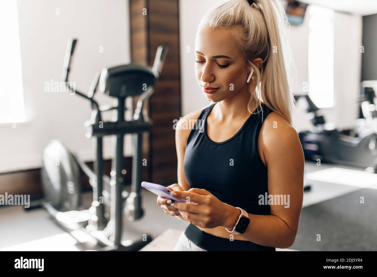 Hermosa mujer joven fitness, en ropa deportiva, relajarse después de un entrenamiento utiliza un teléfono móvil, en el gimnasio Fotografía de - Alamy