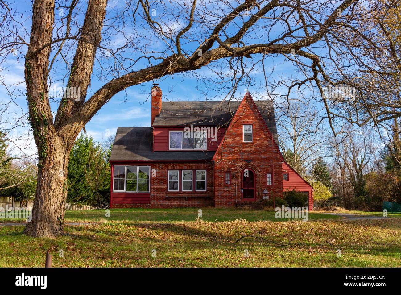 Rockville, MD, EE.UU. 11-10-2020: Una casa vintage de ladrillo rojo de dos pisos en una amplia tierra con un árbol alto en su patio delantero. Un buen ejemplo de un histo Foto de stock