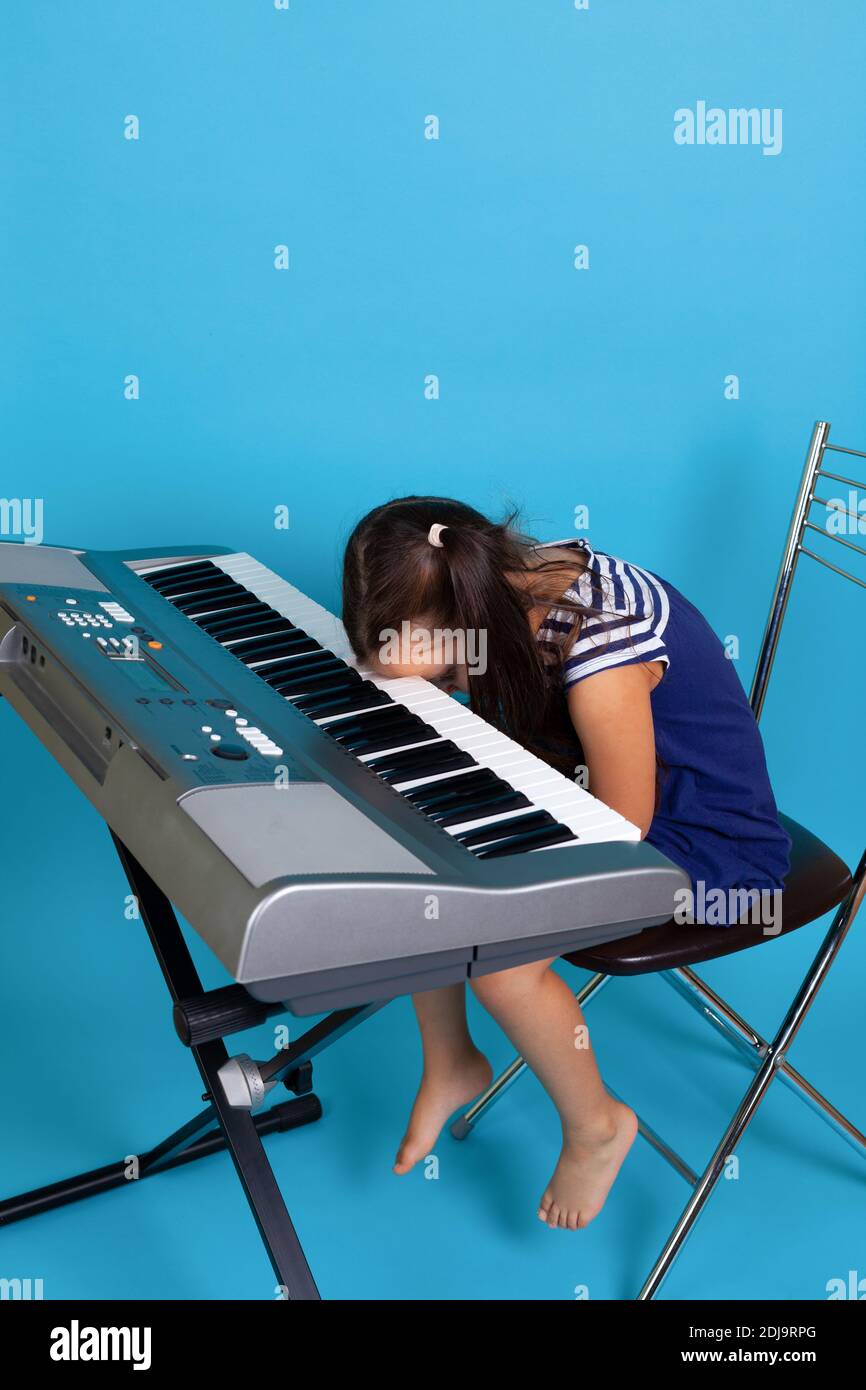 una chica llorando se sienta al piano y se inclina la cabeza hacia las  teclas, odiando la escuela de música, aislada sobre un fondo azul  Fotografía de stock - Alamy