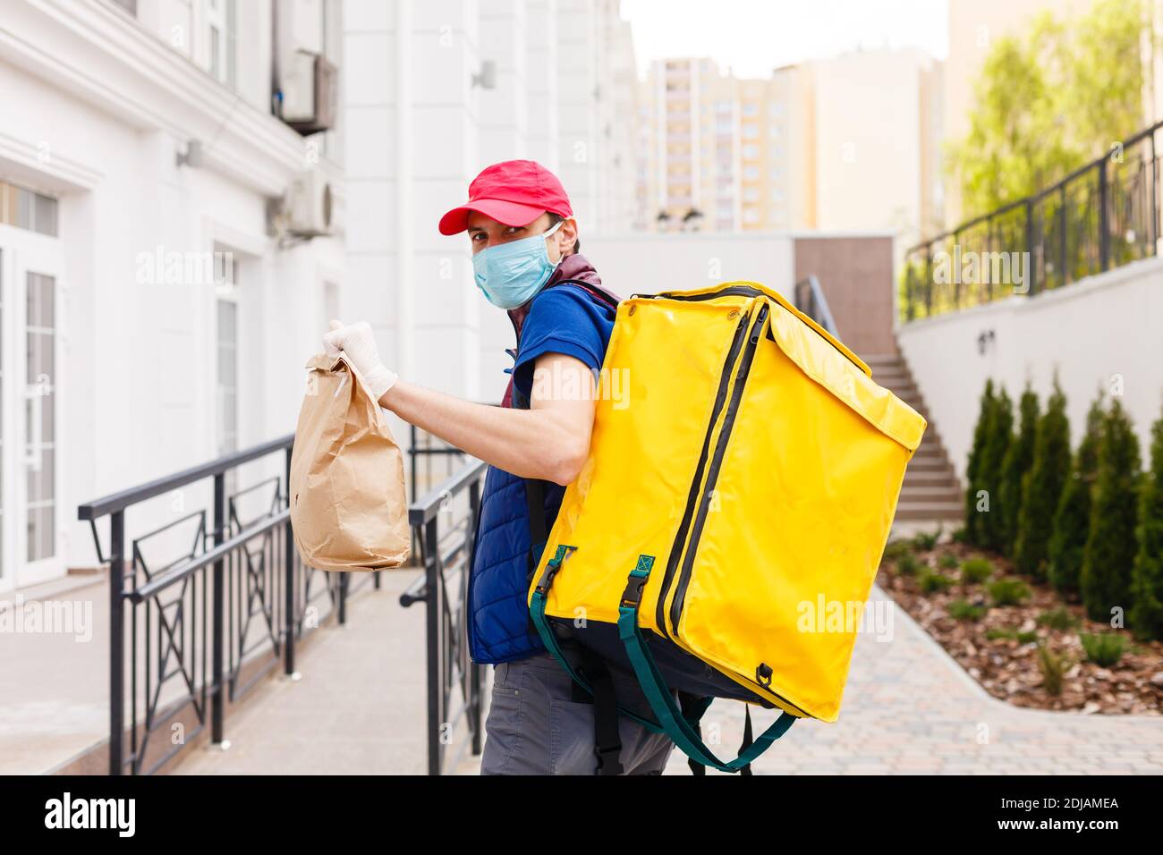Retrato de un hombre de pie con entrega alegre amarillo Mochila térmica para la entrega de alimentos en la calle al aire libre Foto de stock