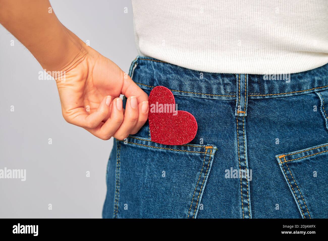 mujer sosteniendo un pequeño corazón rojo brillante poniéndolo o quitándose el bolsillo de sus jeans. Compartiendo y recibiendo San Valentín, guardando amor en ti Foto de stock
