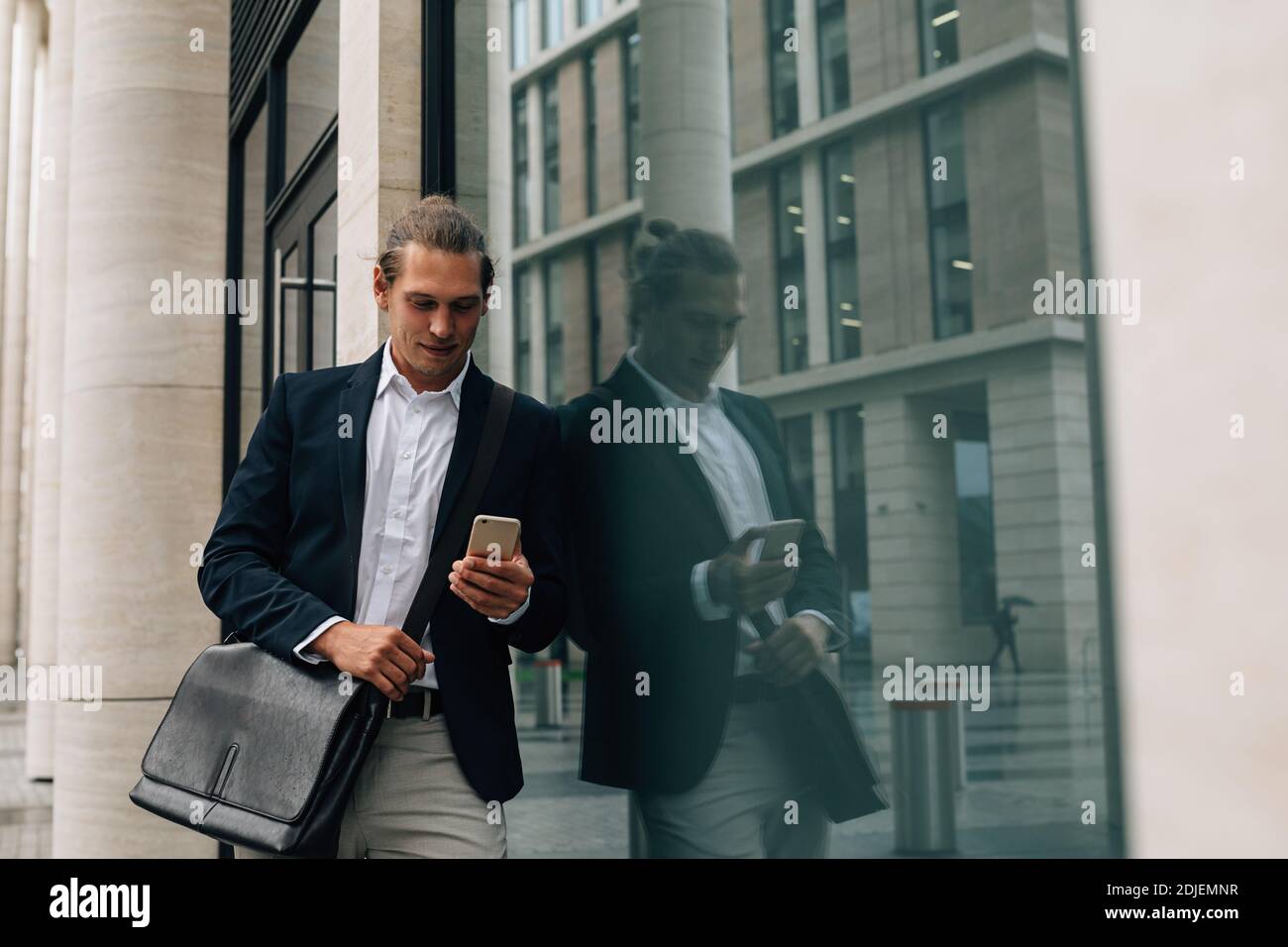 Hombre de negocios con ropa formal mirando el smartphone de pie en la oficina edificio Foto de stock