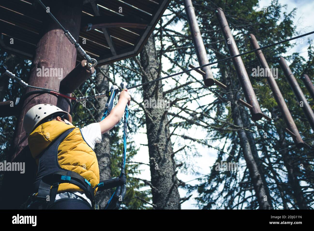 Debajo de la vista del arnés de seguridad de sujeción para niños en tirolina  mientras se encuentra de pie en la copa de los árboles en Adventure Park  Fotografía de stock -