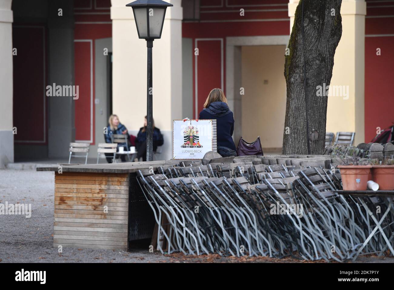 Foto del tema: Pandemia de coronavirus/consecuencias para la gastronomía. Algunos transeúntes, la gente se sienta al lado de mesas y sillas plegadas y bebe su café para ir. Mesas y sillas juntas en la zona exterior de un restaurante en el Hofgarten en Munich el 14 de diciembre de 2020. A partir del 16 de diciembre de 2020, se iniciará un cierre de emergencia hasta el 10 de enero, la restauración debe permanecer cerrada, consecuencia del cierre de la pandemia de corona, bloqueo, cierre, valor de incidencia. | uso en todo el mundo Foto de stock