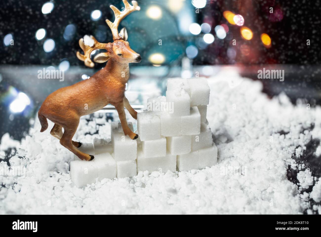 Escena de renos decorativos sobre nieve artificial y cubos de azúcar Con un bokeh luces de Navidad de fondo Foto de stock