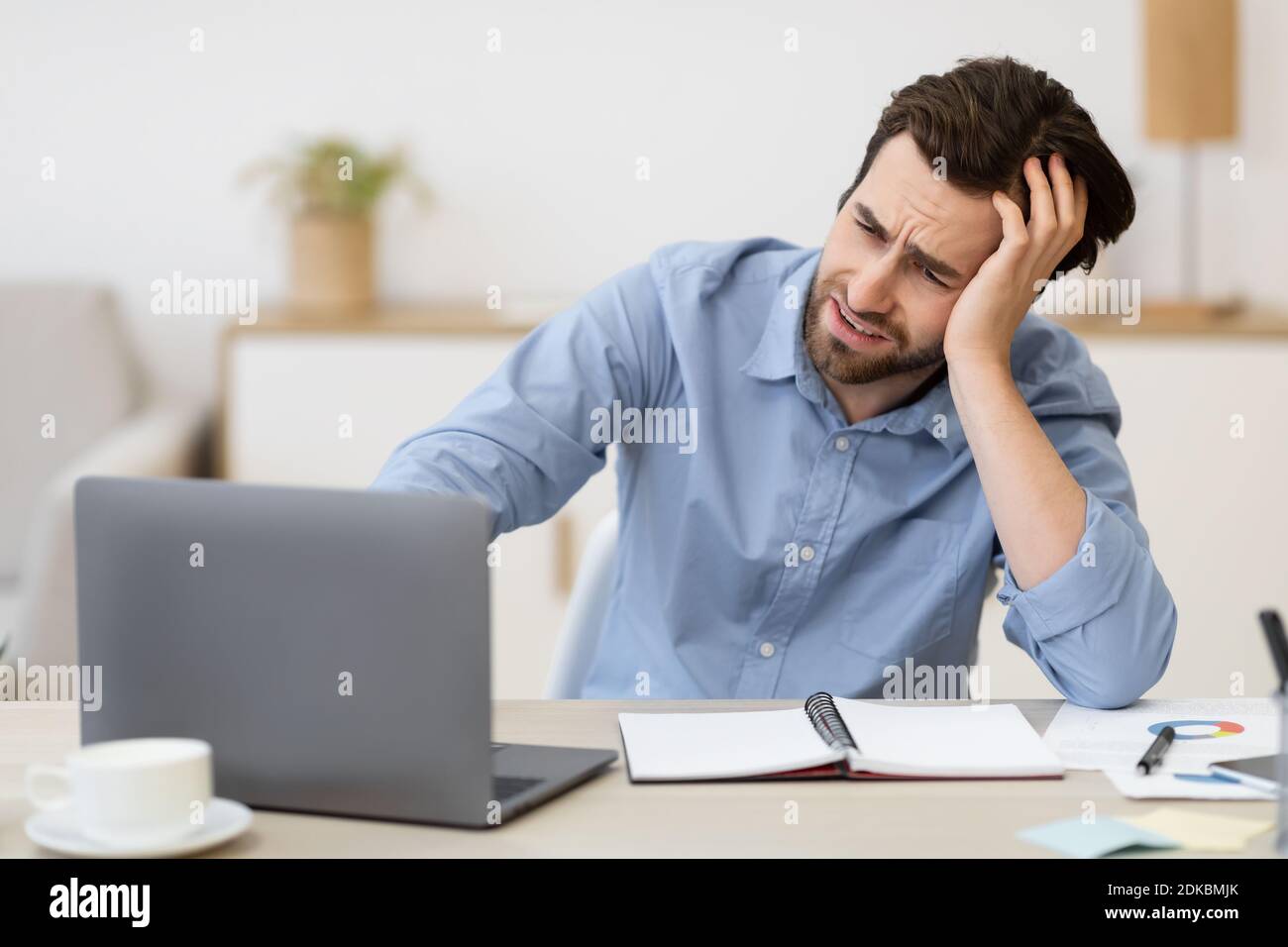 Hombre infeliz sentado en el ordenador portátil mirando la pantalla en el lugar de trabajo Foto de stock