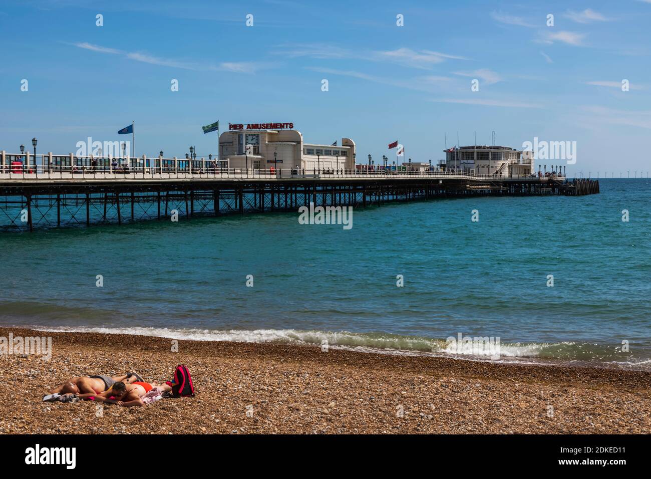 Inglaterra, West Sussex, Worthing, Worthing Beach, Pareja tomando el sol en la playa con Pier en el fondo Foto de stock