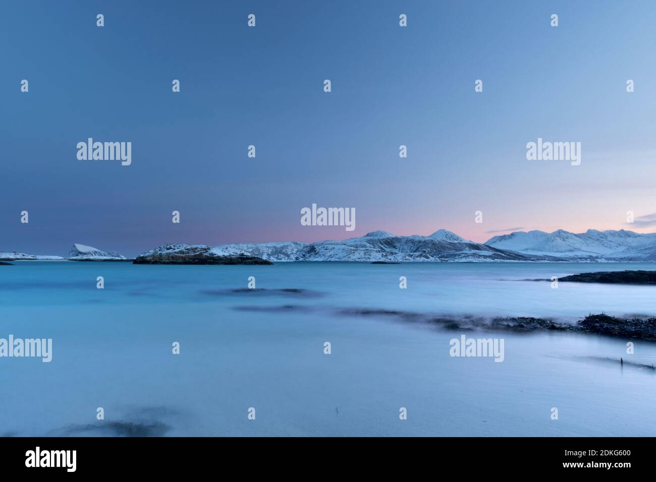 Amanecer helado en la isla de Sommaroy en invierno con una vista Desde la playa del Mar del Norte de Europa y el montañas nevadas en el horizonte Foto de stock
