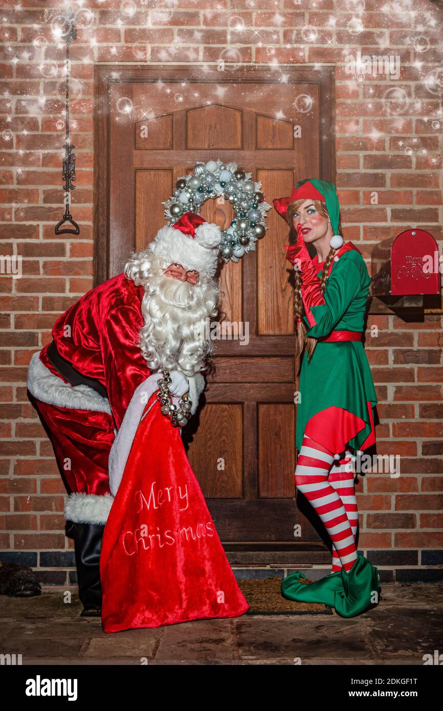 Reino Unido, Quorn - 2020 de diciembre: Santa y un Elf se colan a una puerta principal mientras entregan regalos de un gran saco rojo Foto de stock
