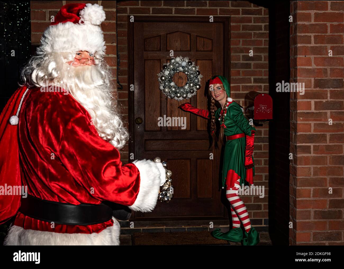 Reino Unido, Quorn - Diciembre 2020: Santa y un Elf se colan en una puerta principal mientras entregan regalos Foto de stock