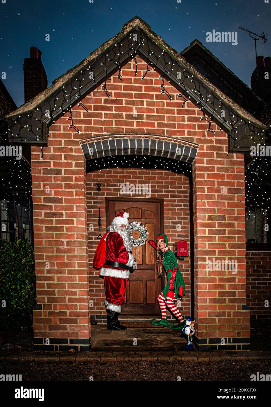 Reino Unido, Quorn - Diciembre 2020: Santa y un Elf se colan en una puerta principal mientras entregan regalos Foto de stock