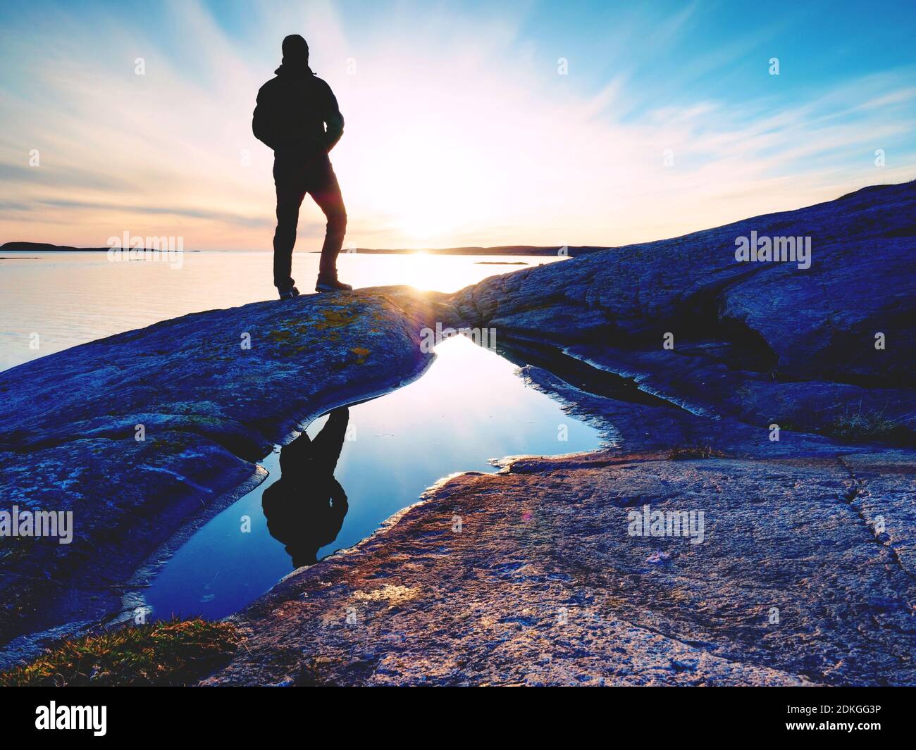 Caminante hombre en ropa deportiva oscuro con mochila deportiva en costa rocosa. mochilero en de agua de pie en Boulder y disfrutar del atardecer en horizonte con blu Fotografía