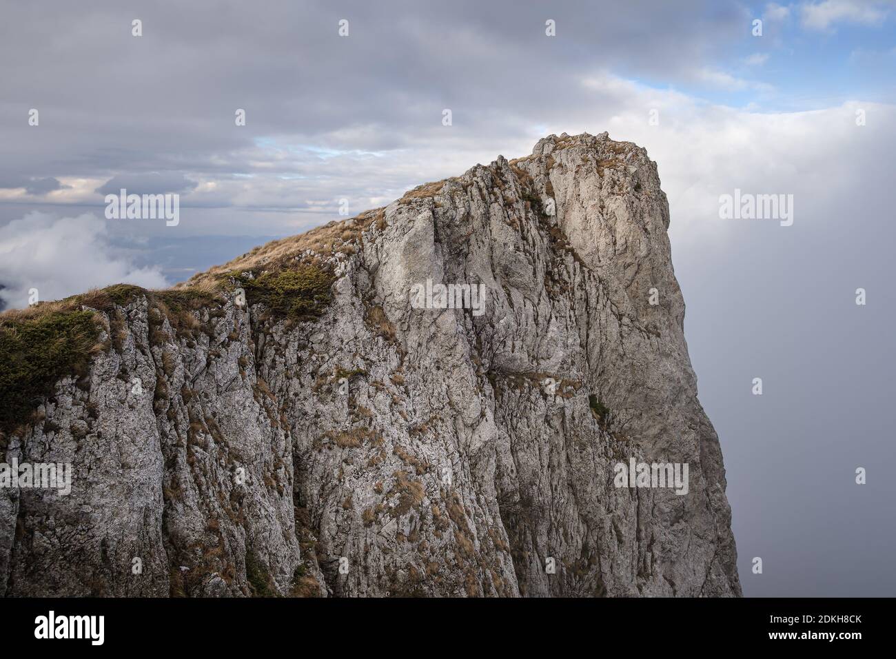 Acantilado rocoso, empinado, vertical en la montaña seca (Suva planina) cubierto de hierba seca, naranja en otoño y cielo azul nublado Foto de stock