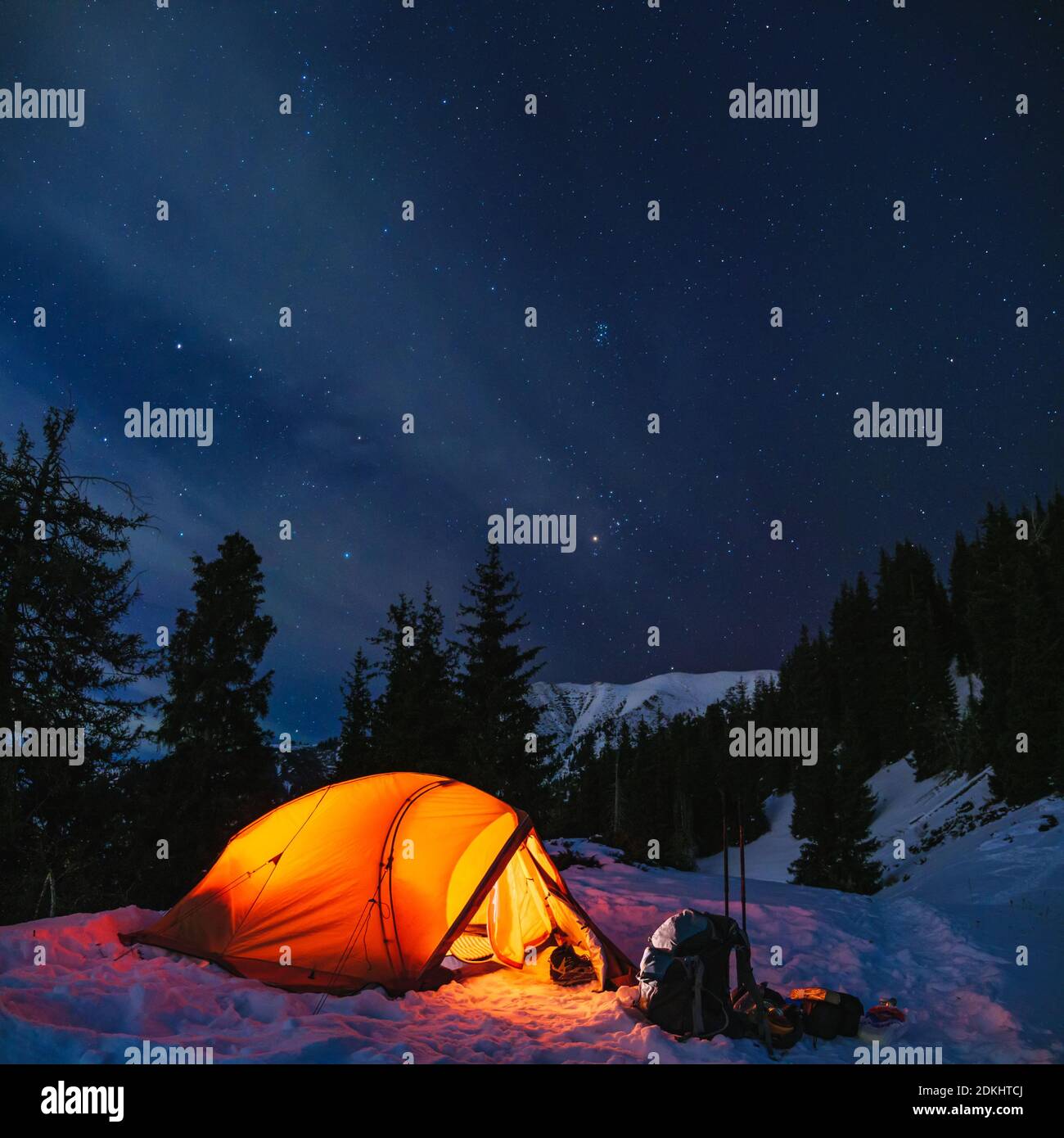 Paisaje nocturno de invierno de montaña con carpa naranja. Senderismo con una estancia de una noche en las montañas en invierno Foto de stock