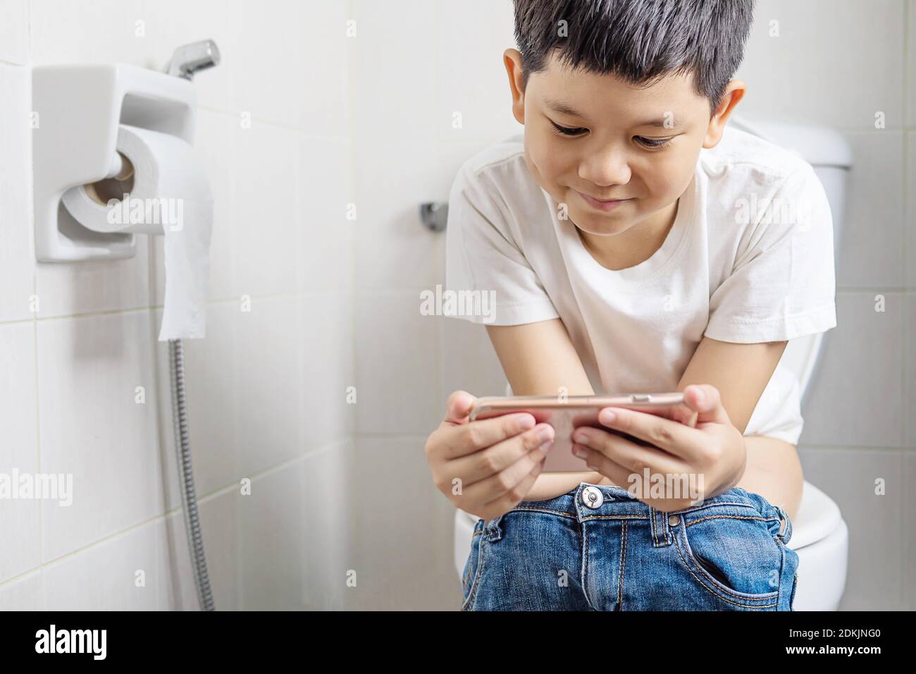Niño usando el teléfono móvil mientras está sentado en el inodoro del  cuarto de baño Fotografía de stock - Alamy