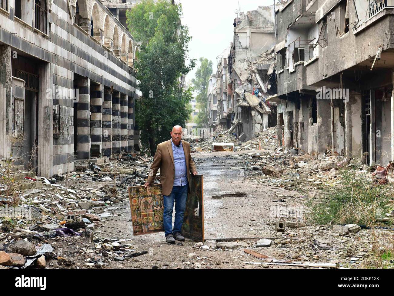Campamento de Yarmouk, Siria. 26 de noviembre de 2020. El artista palestino Mohammad al-Rakoui lleva pinturas en el campamento de Yarmouk en el sur de Damasco, Siria, el 26 de noviembre de 2020. Al igual que un paramédico que buscaba supervivientes atrapados bajo los escombros, Mohammad al-Rakoui estaba buscando pinturas enterradas en los escombros de su estudio devastado en el campamento de Yarmouk, devastado por la guerra. Crédito: Ammar Safarjalani/Xinhua/Alamy Live News Foto de stock