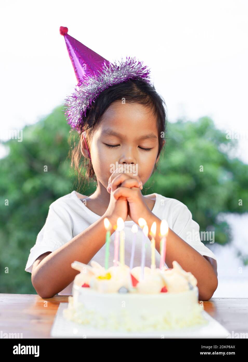 Niña de cumpleaños que desea mientras lleva sombrero de fiesta en casa  Fotografía de stock - Alamy