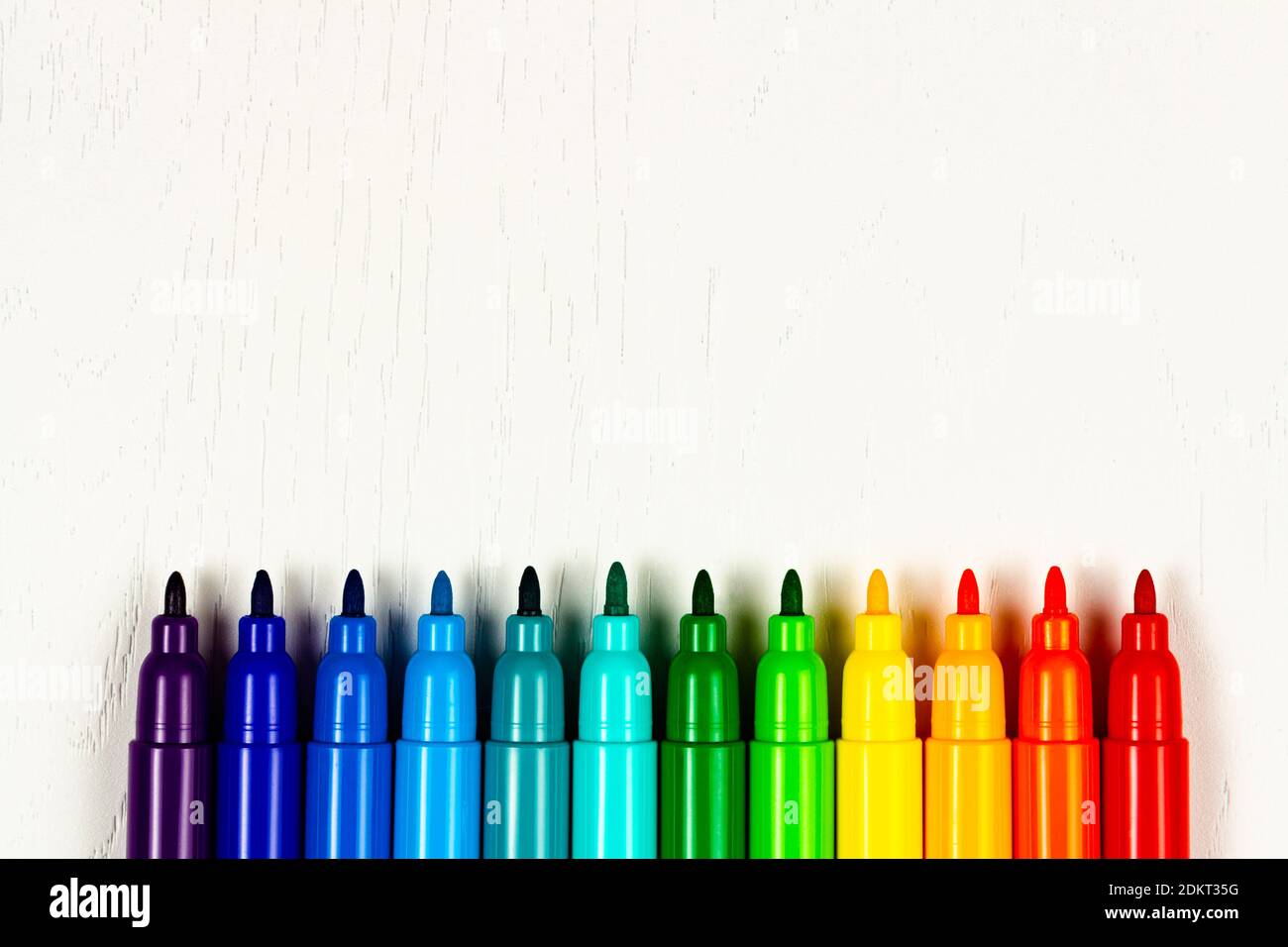 los marcadores de colores brillantes sin tapas se encuentran en una madera blanca tabla Foto de stock