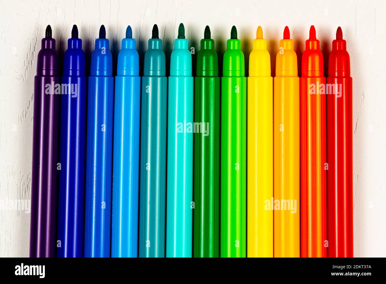 los marcadores de colores brillantes sin tapas se encuentran en una madera blanca tabla Foto de stock