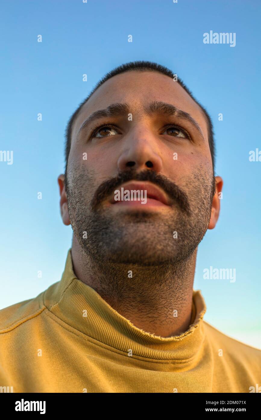 Retrato de un joven con bigote mirando hacia arriba de cielo azul con puente amarillo Foto de stock