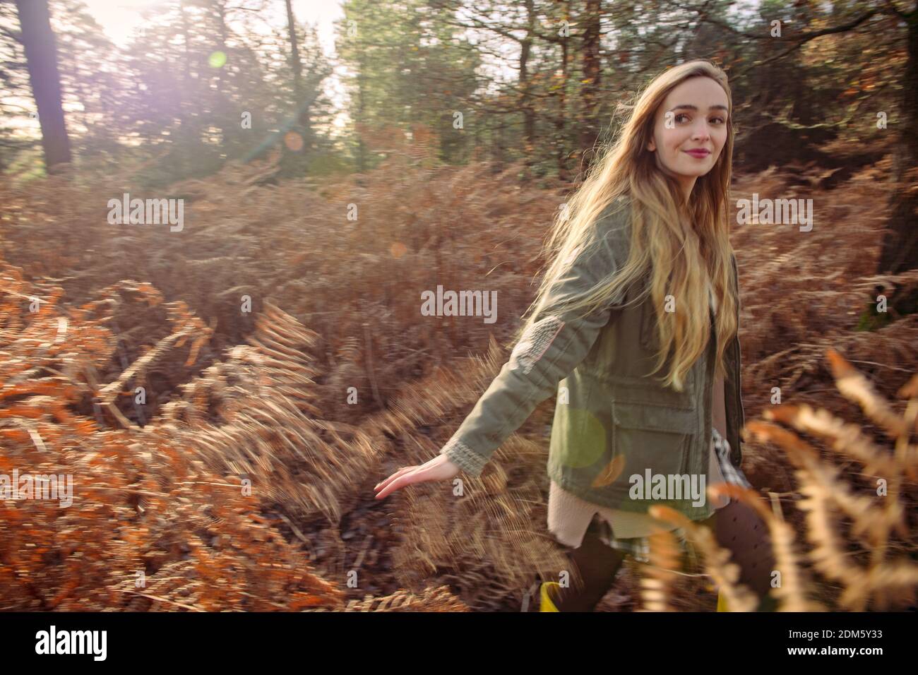 Una mujer joven y natural (20 años) corre por los helechos otoñales y se divierte en un entorno de bosque con una sensación de movimiento en un día soleado. Foto de stock