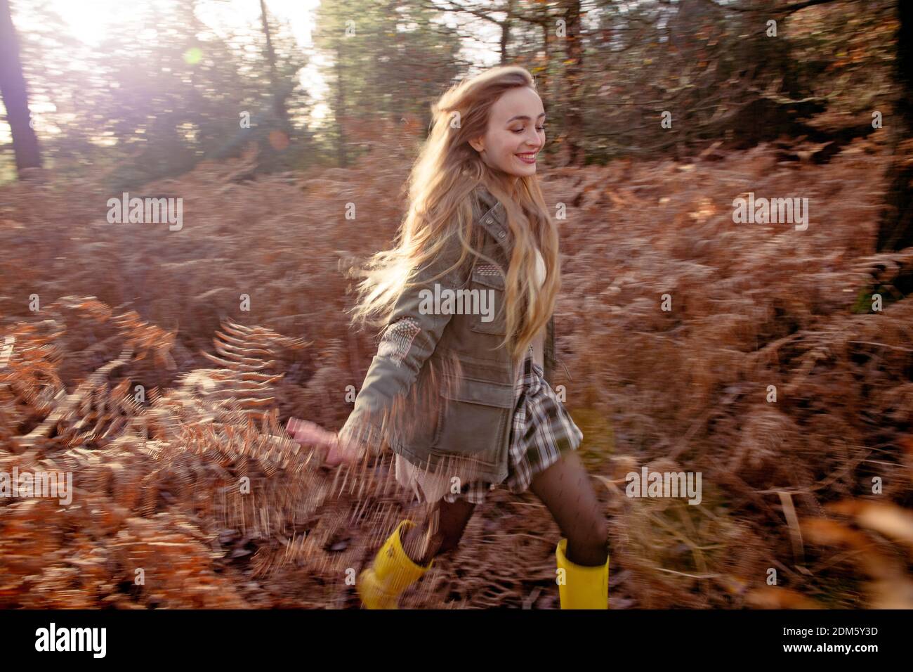 Una mujer joven y natural (20 años) corre por los helechos otoñales y se divierte en un entorno de bosque con una sensación de movimiento en un día soleado. Foto de stock