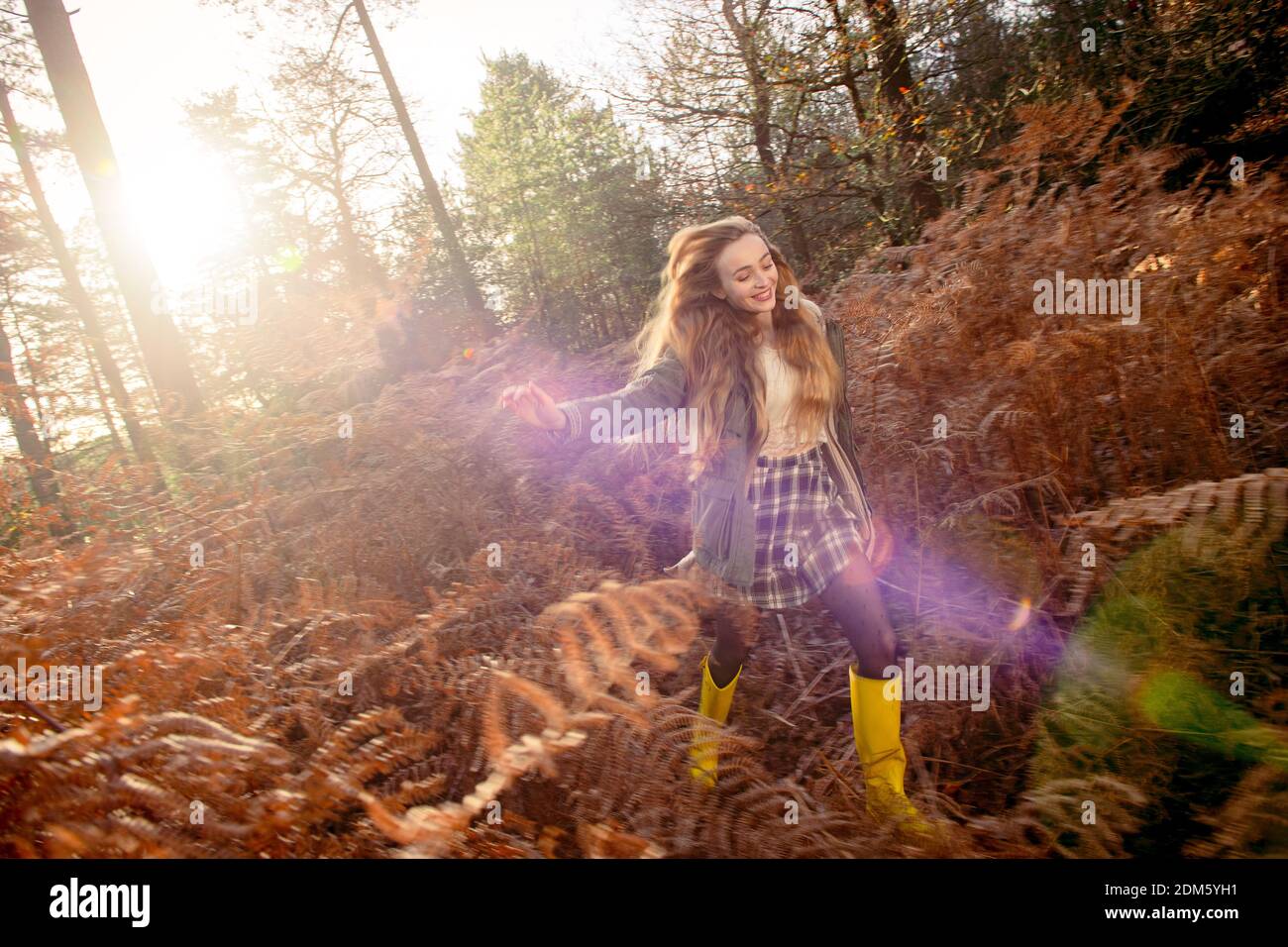 Una mujer joven y natural (20 años) corre por los helechos otoñales y se divierte en un entorno de bosque con una sensación de movimiento en un día soleado. Foto de stock