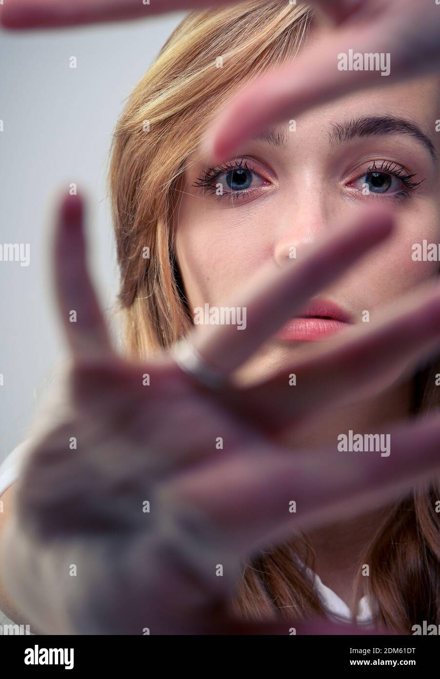 Las mujeres jóvenes hermosas (20 años) sostiene las manos a la cámara para crear un primer plano y los compañeros a través de sus dedos que la atención a sus ojos. Foto de stock