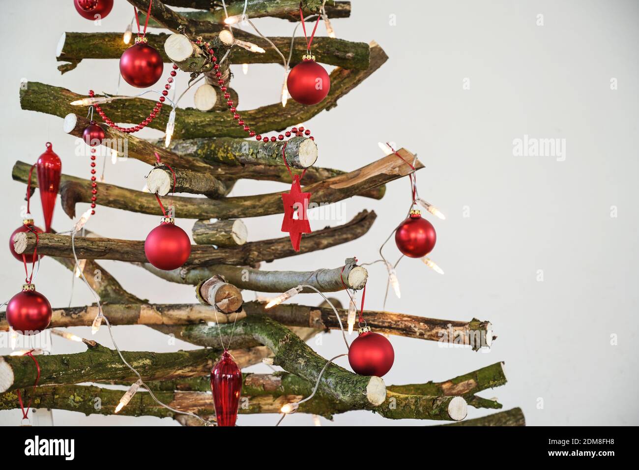 Árbol de Navidad rústico hecho en casa de ramas de madera cruda, decorado  con luces de hadas y bolas rojas, alternat sostenible y respetuoso con el  medio ambiente Fotografía de stock -