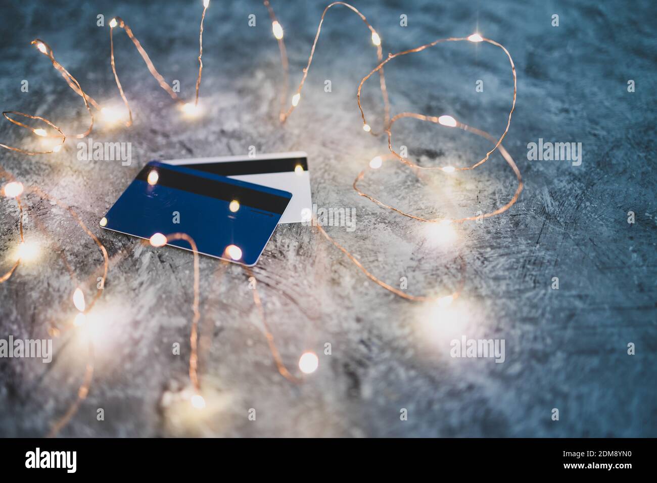 compras y consumismo imagen conceptual, tarjetas de crédito en un escritorio de concreto rodeado de brillantes luces de hadas Foto de stock