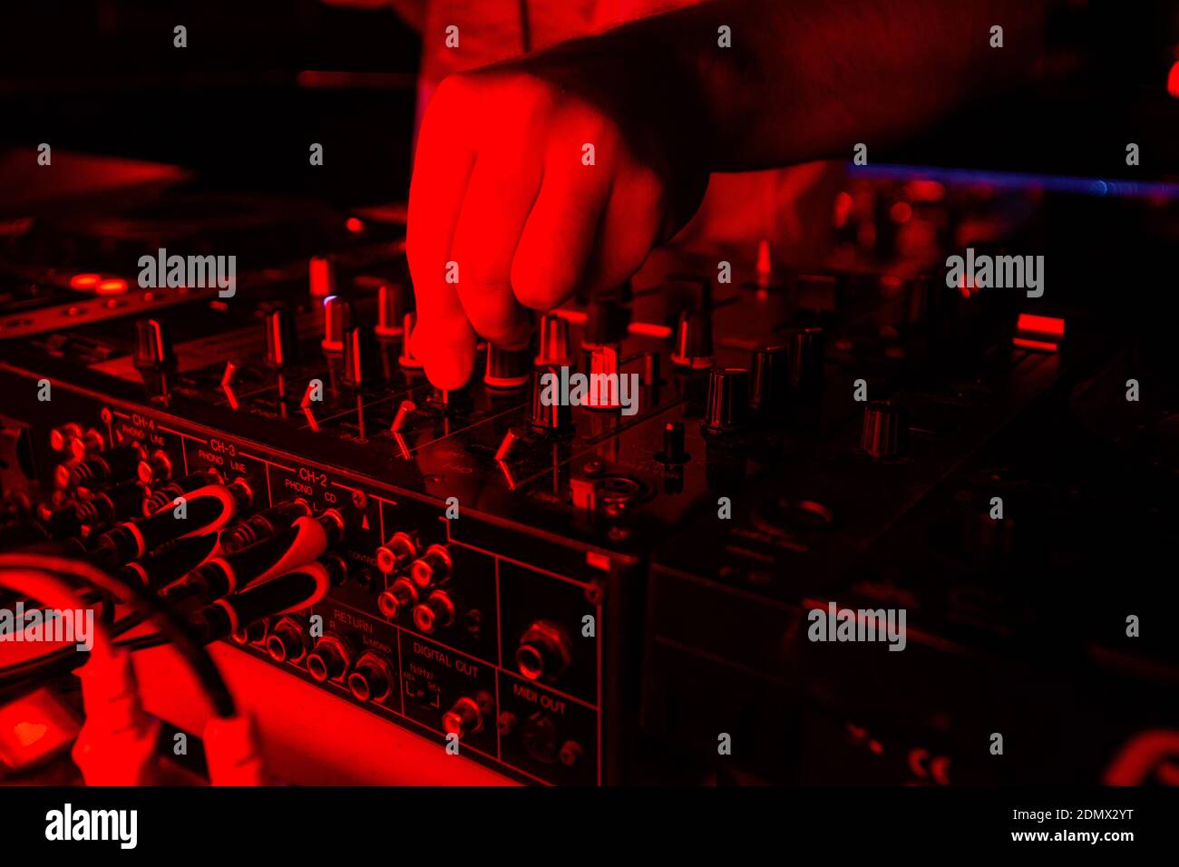 Mezclador de DJ con luz roja brillante. Corte un tiro de cerca de la mano  masculina girando vasos en la consola de jockey de disco. Concepto de vida  nocturna. Fiesta rave con