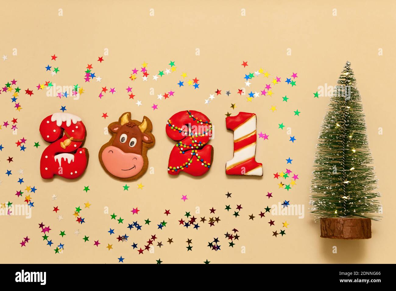 Números 2021 de galletas de pan de jengibre en esmalte multicolor sobre fondo beige. El símbolo del toro de año, estrellas multicolores y una Navidad tr Foto de stock