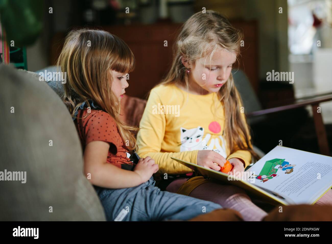 Hermanas leyendo libro en el sofá Foto de stock