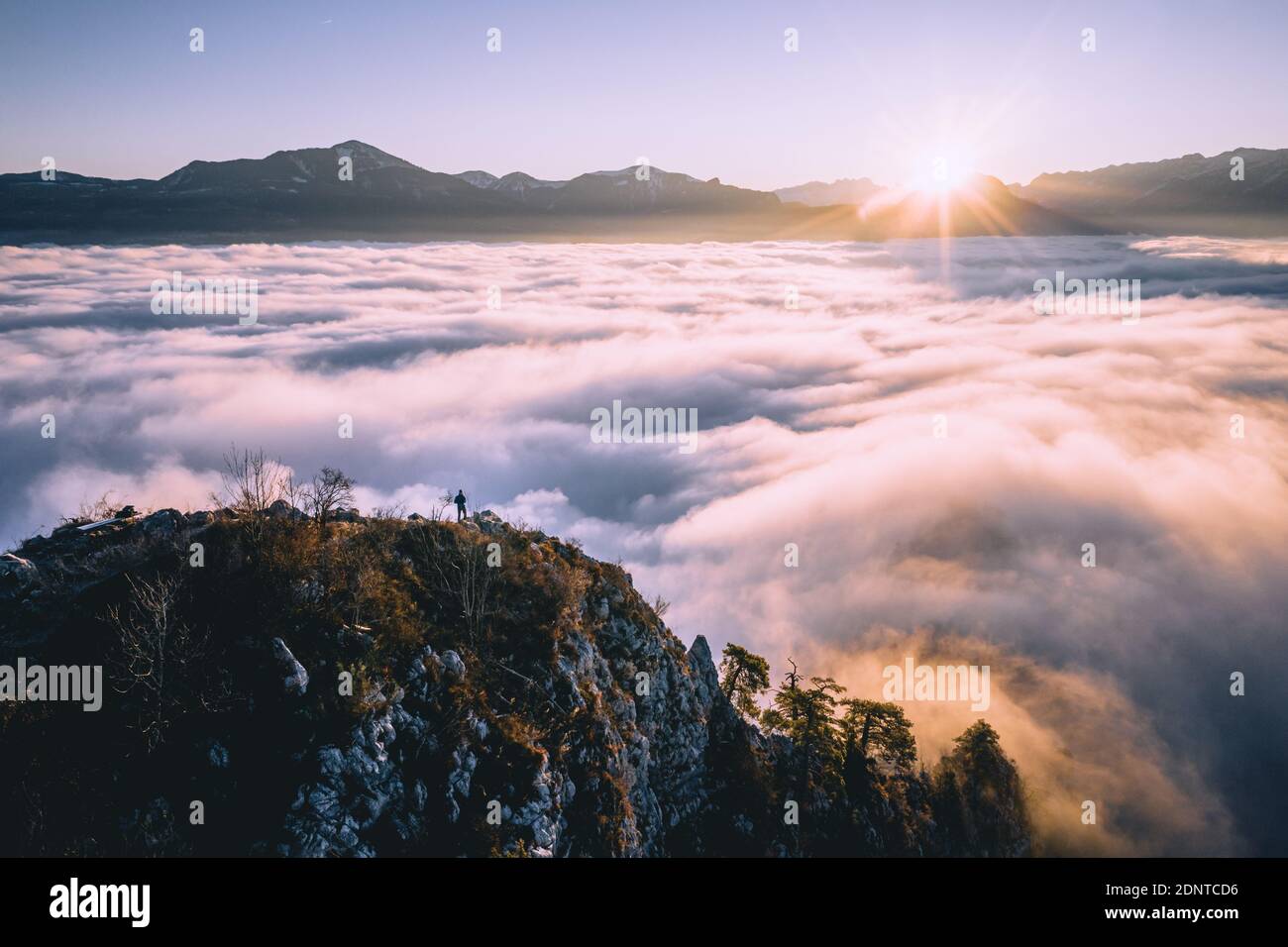 Hombre de pie en la cresta de la montaña que se eleva por encima de la alfombra de nubes, Hallein, Salzburgo, Austria Foto de stock