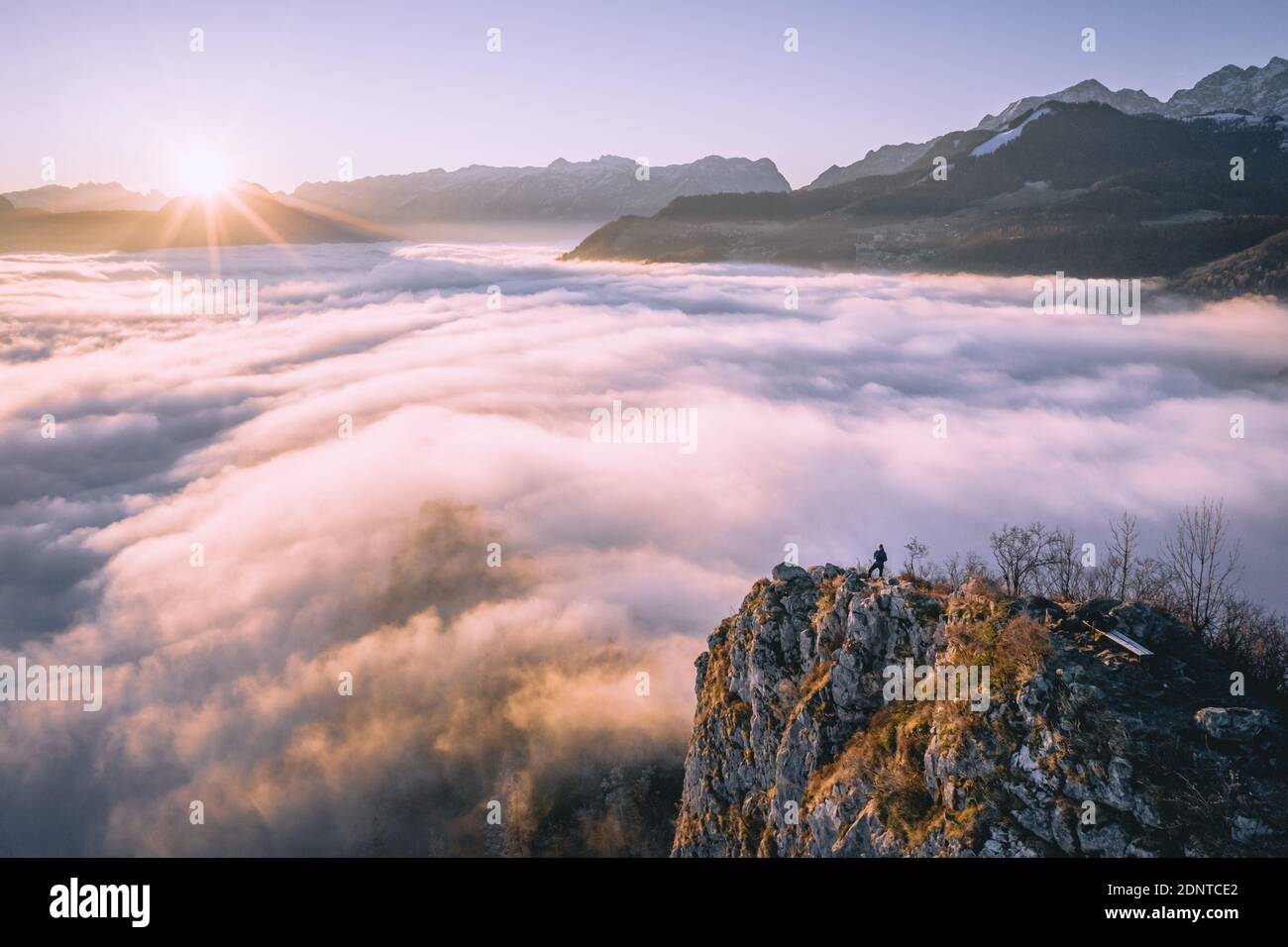 Hombre de pie en la cresta de la montaña que se eleva por encima de la alfombra de nubes, Hallein, Salzburgo, Austria Foto de stock