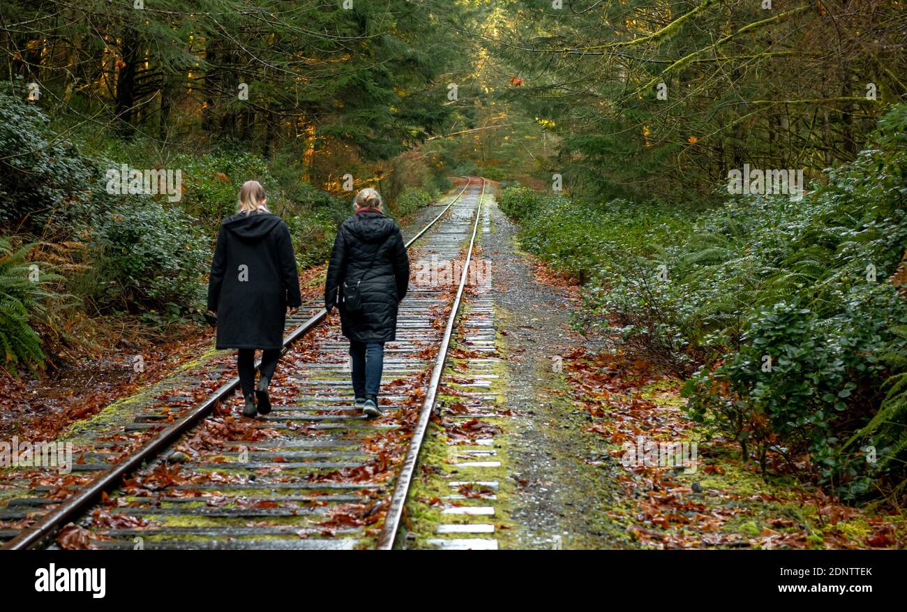 Vista posterior de una madre e hija caminando por una vía férrea en otoño, Goldstream, Isla de Vancouver, Canadá Foto de stock