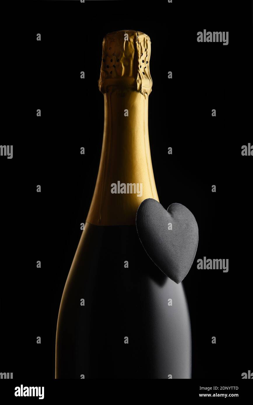 Concepto del día de San Valentín: Primer plano de una botella de champán con un corazón negro sobre un fondo negro. Foto de stock