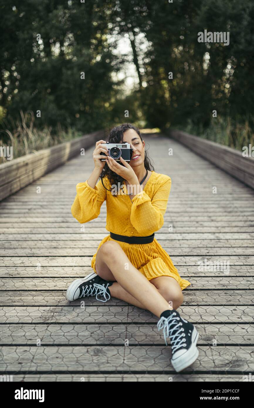 Joven fotógrafo vistiendo vestido amarillo y negro zapatillas sosteniendo  una cámara analógica en el paseo marítimo de madera Fotografía de stock -  Alamy
