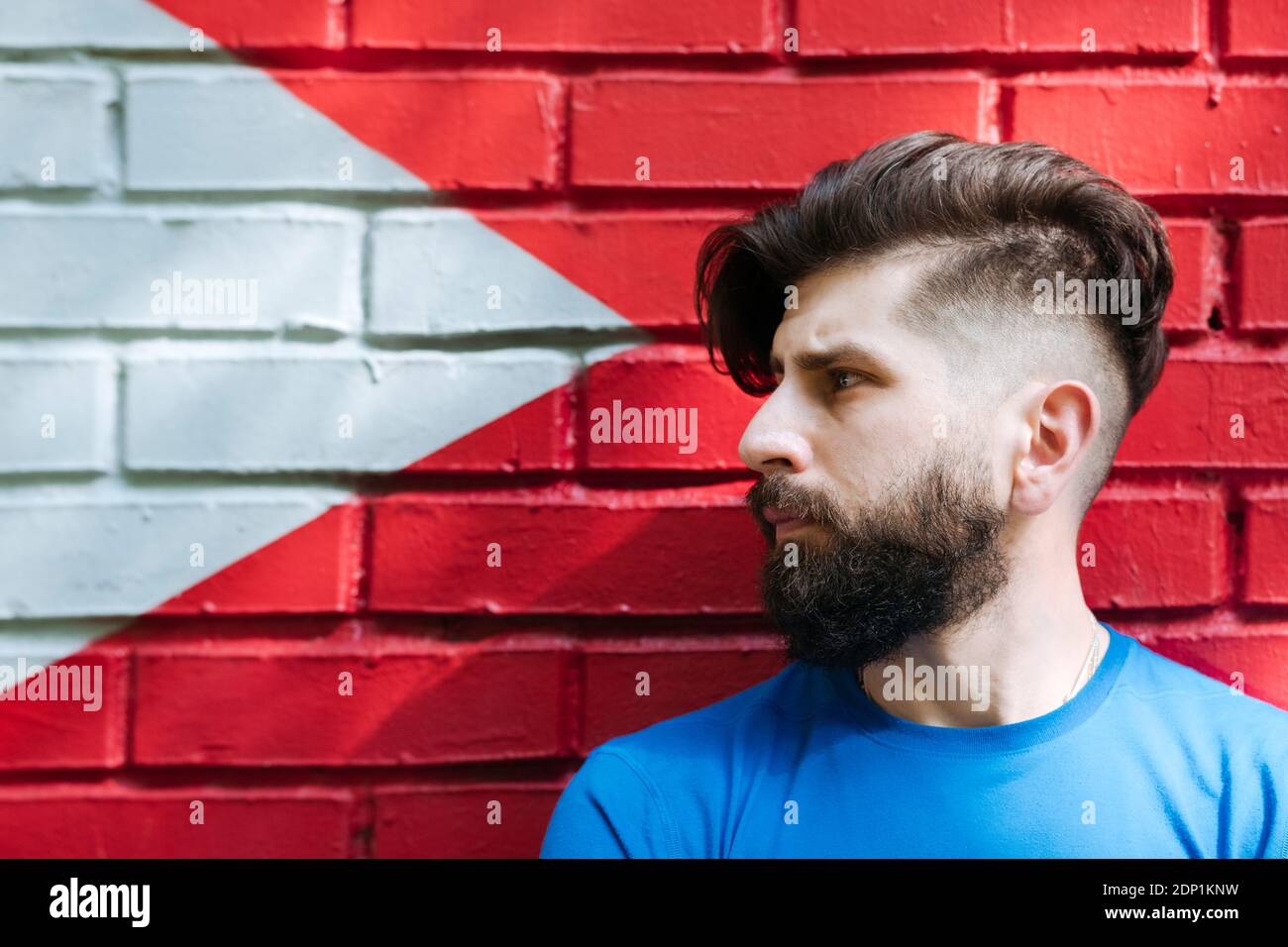 Hombre joven con tatuaje de pie frente a la pared de ladrillo rojo, retrato Foto de stock